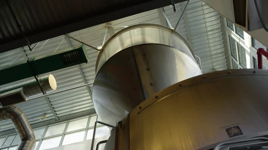 A large steel machine in a warehouse with piping and windows