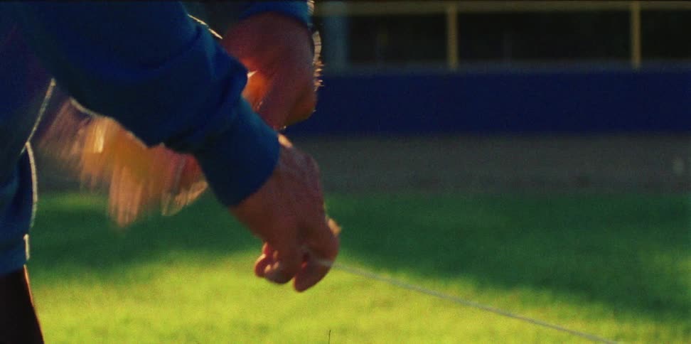 A man unrolls a ball of twine on an athletic field