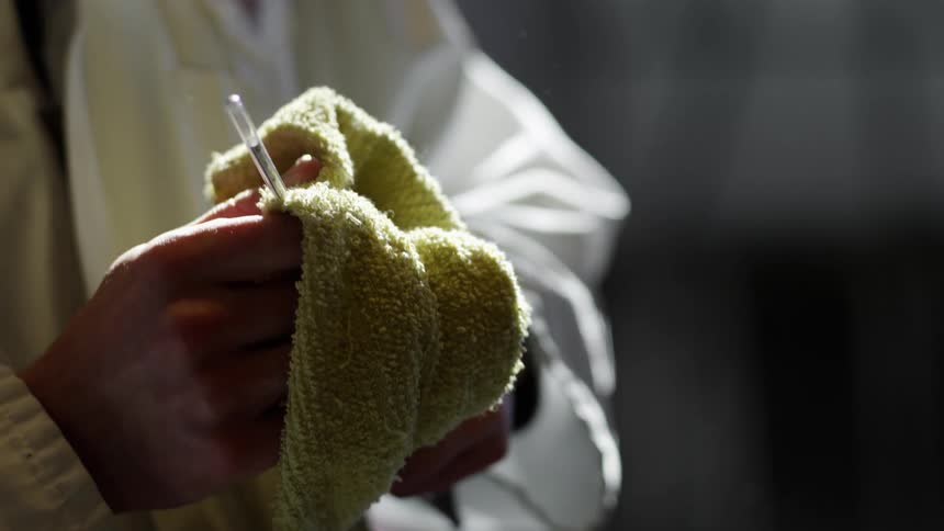 A male lab worker wipes a pipette with a yellow towel