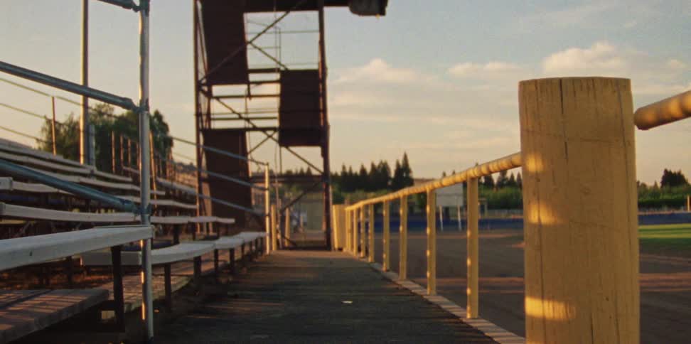 Bleachers with a yellow railing and a metal staircase at the end of the seating adjacent to a sporting field