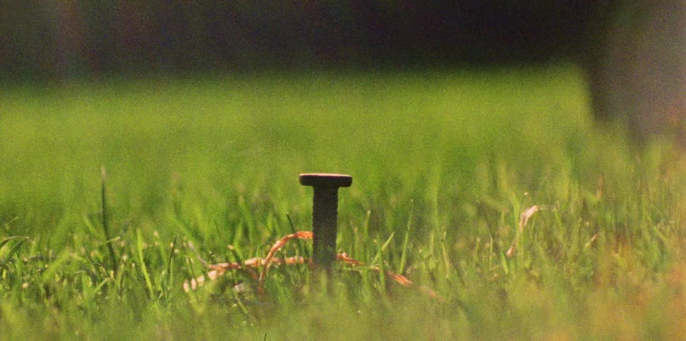 A man nails a nail into the grass