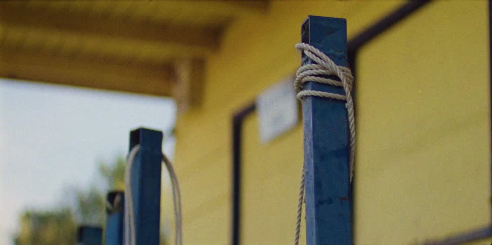 Metal poles have ropes tied through holes in the top in front of a yellow building