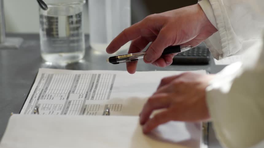 A person with a pen placing it on a book on a table with a calculator