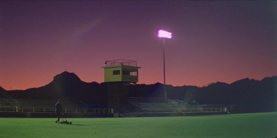 Person works on a football field while the last bit of sun sets behind the bleachers