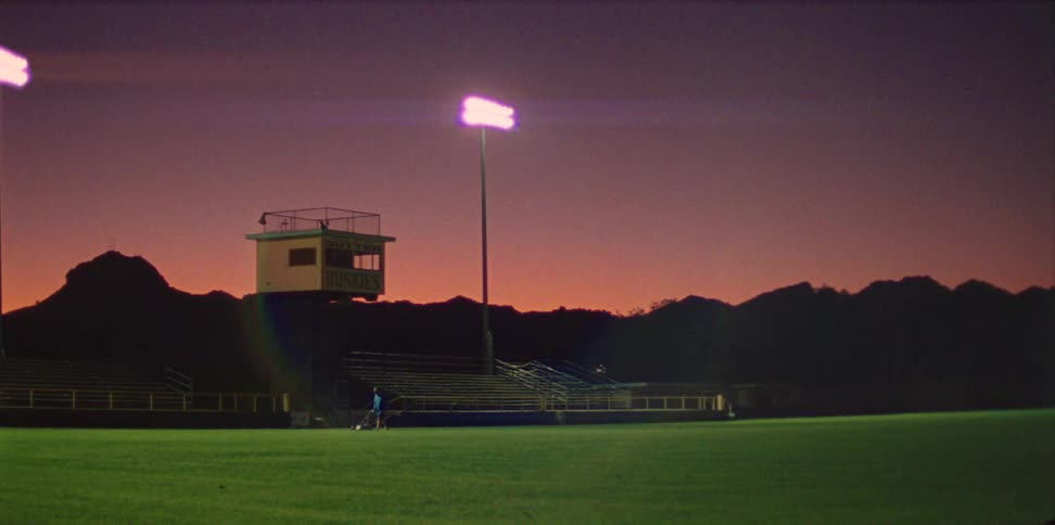 A person in a sports field with bleachers a mountain range the sky and clouds in the background