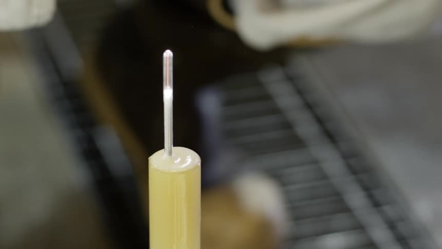 A hand twirls a thermostat in a tube of yellow liquid and leaves it to continue spinning
