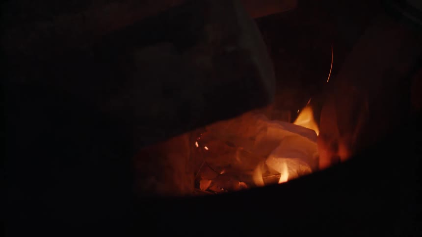A person adding paper to a campfire at night