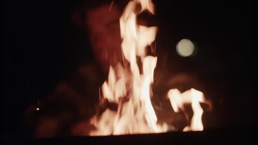 Man sits next to the campfire with the full moon in the night sky behind him