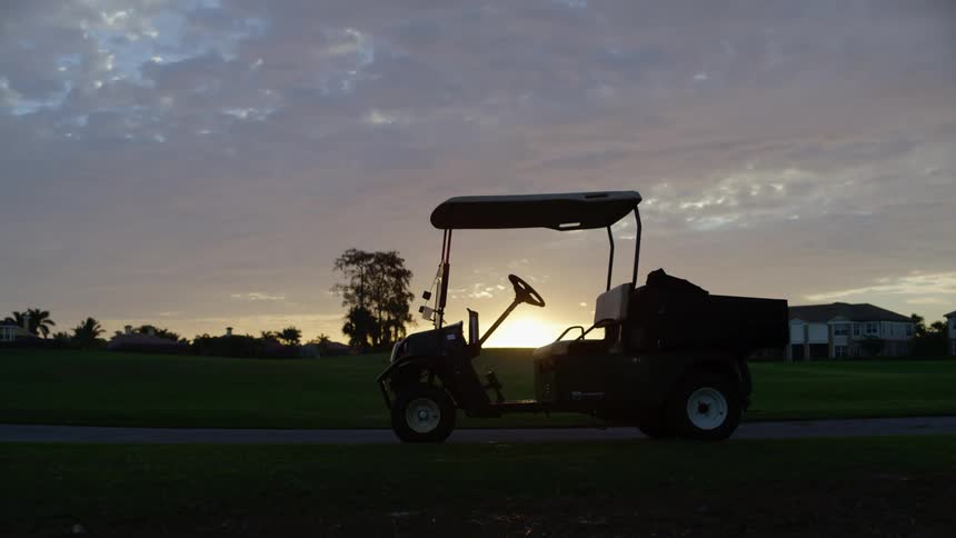 A golf cart parked on a narrow path in a high end neighborhood on a cloudy evening