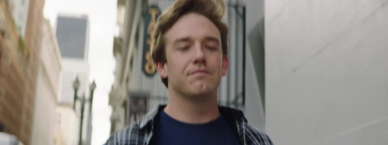 A white male walks down a city street surrounded by buildings