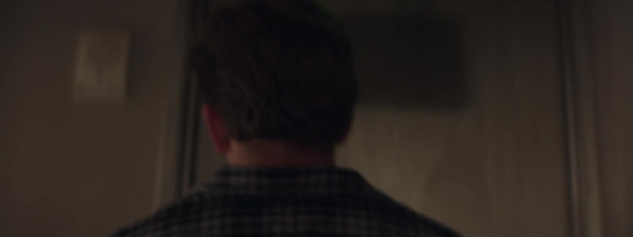 A man walks down a dark hallway and opens the door to his brightly lit office