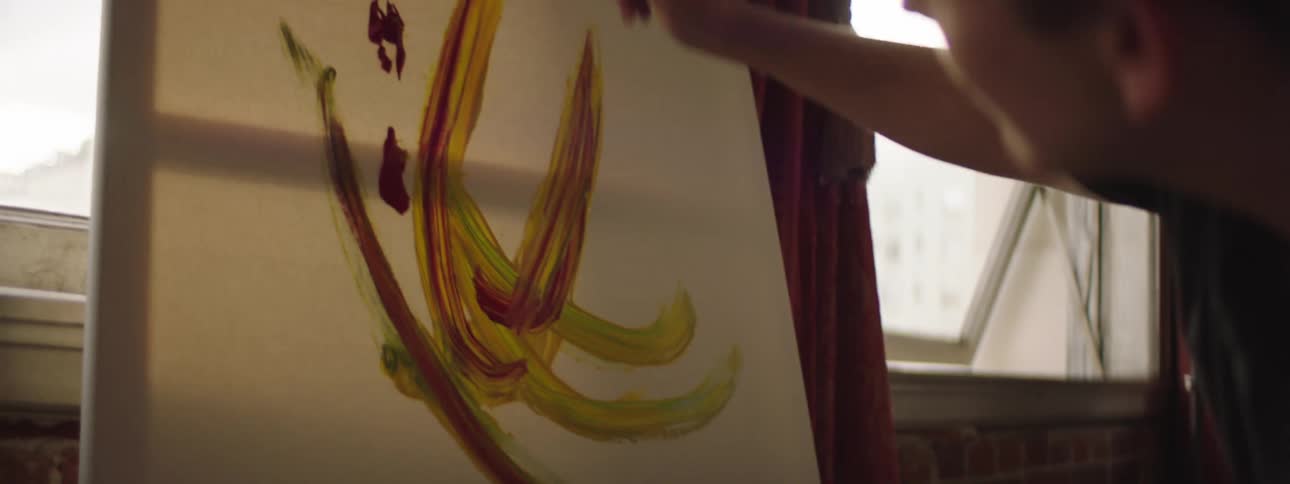 A man with a paintbrush painting on a canvas next to a window