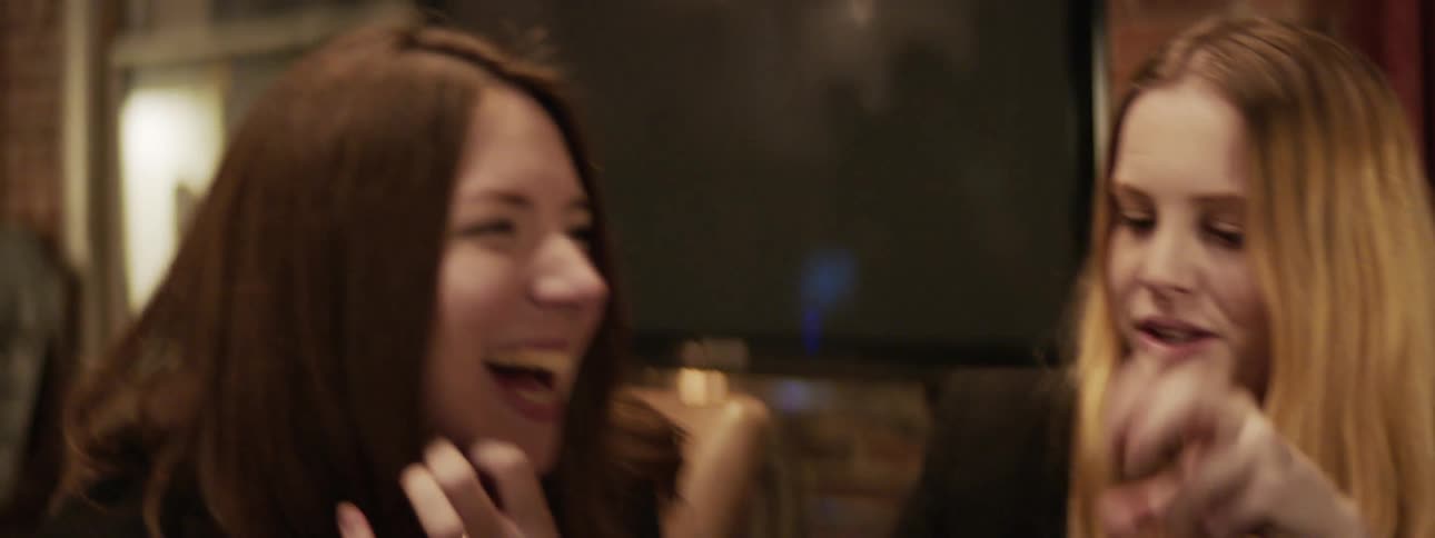A group of men and woman sit at a restaurant table laughing with drinks in hand