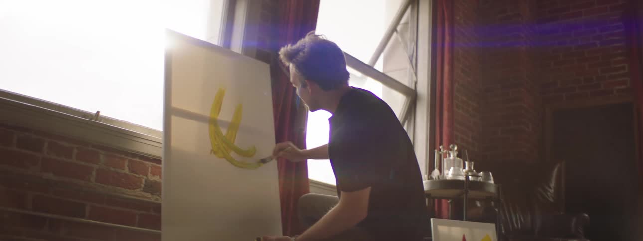 Caucasian man kneeling on a tarp painting on a canvas in a studio