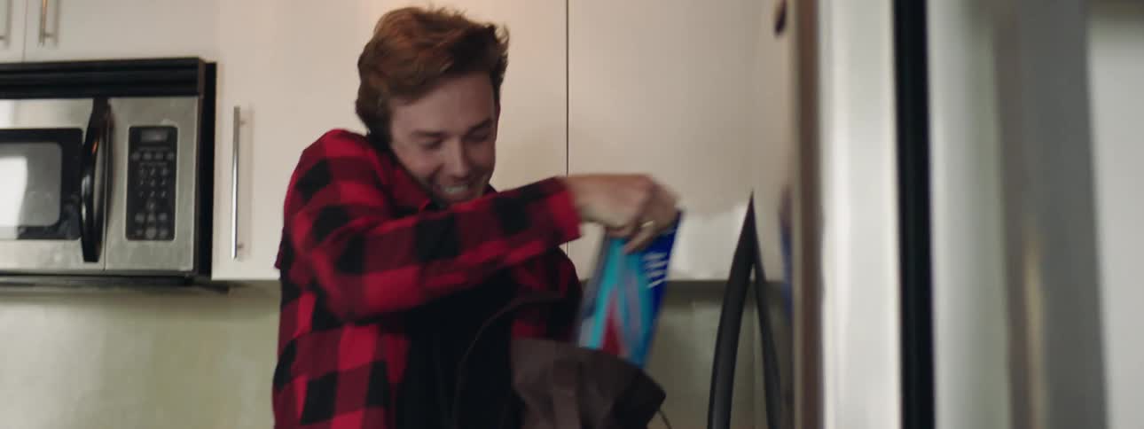 A young man walks in to his home while talking on the cell phone and unpacks a bag of groceries