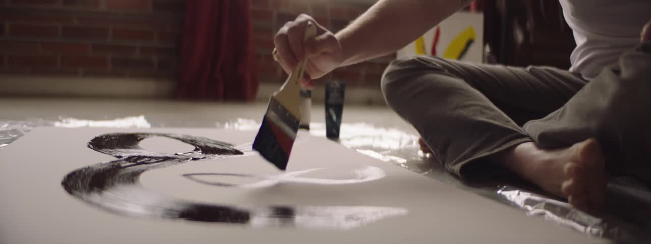 A man sitting on the floor painting a picture on a canvas in his home