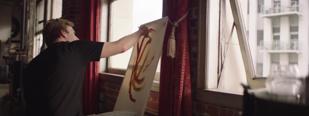 A man uses a paintbrush and red paint to paint on a canvas