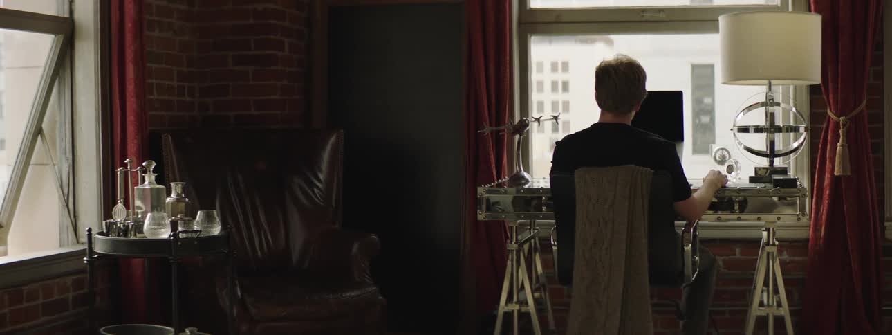 A man uses a computer at a desk in an apartment in a metropolis during the day