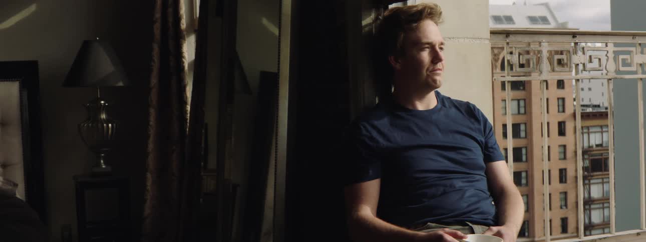 Young man relaxing on the window sill of an apartment in a building
