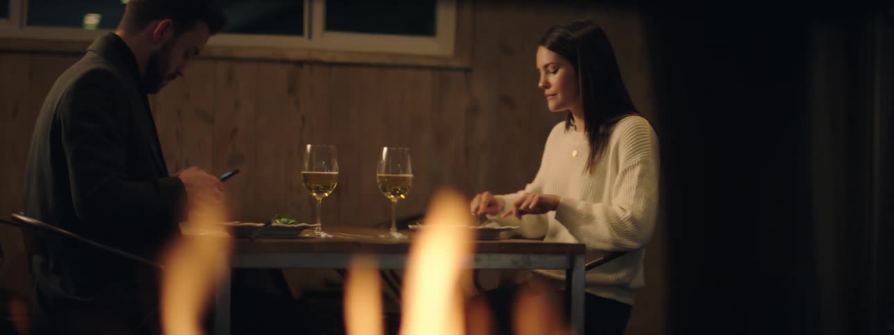 A man eating dinner at restaurant with a woman picks up his cell phone and looks at it