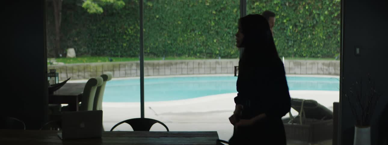 A woman taking a bag from a table with a laptop with a man talking on a smart phone in the background
