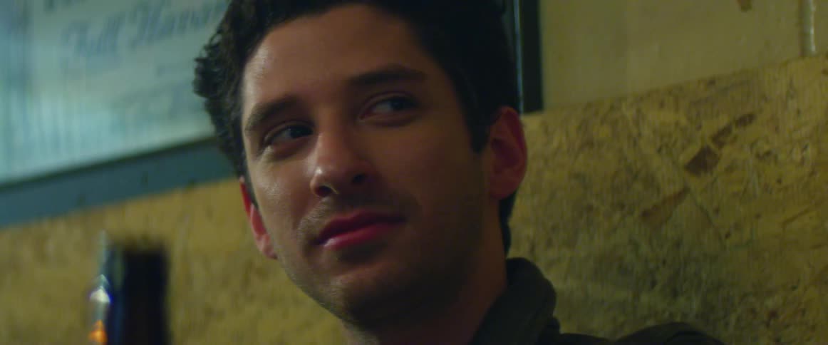 A man sitting in a bar smiles before turning his head to look at something to his left