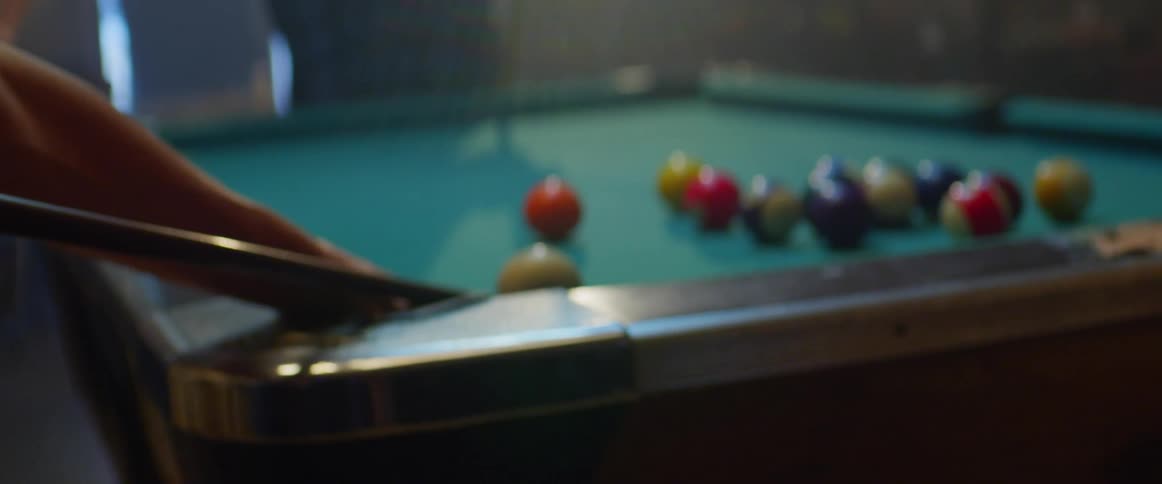 A man shoots pool balls as his friends stand and watch and drink beer