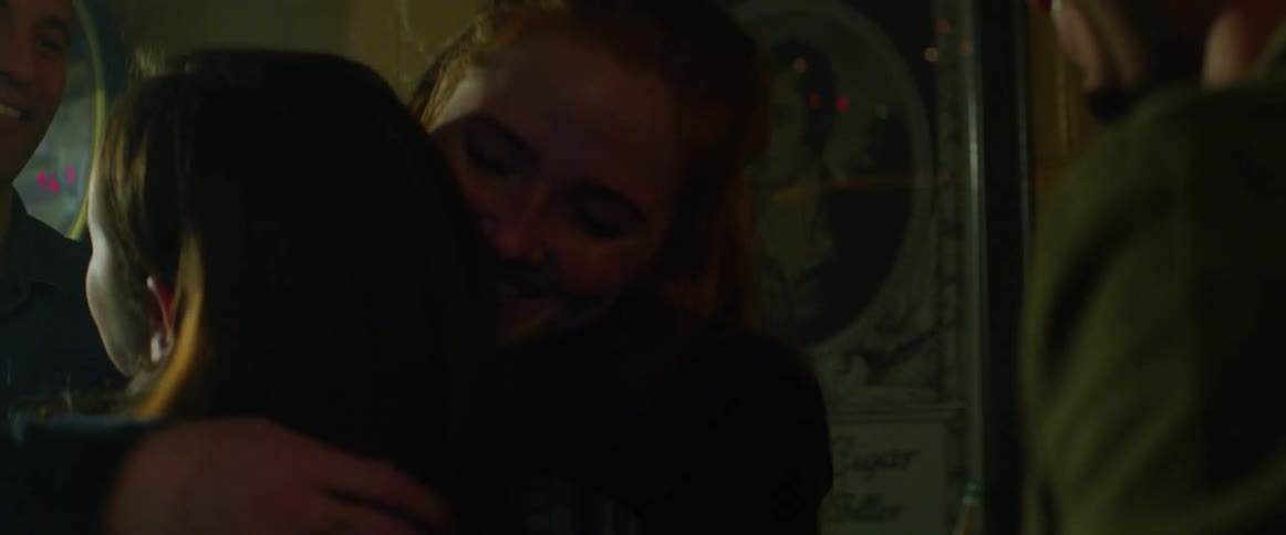 Group of friends greet each other hugging and laughing in a dimly lit bar