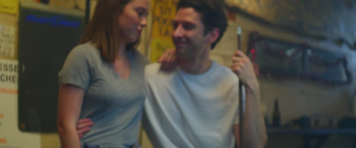 A man shoots a ball in a pool game while another man stands and talks to his girlfriend while waiting for his turn