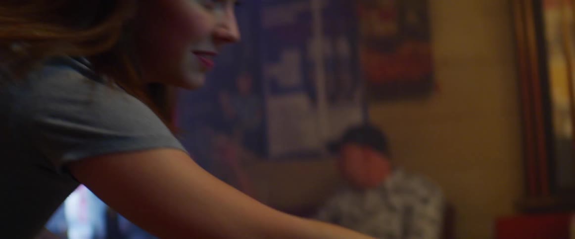A young woman shoot pool in a bar as a young man watches her take a shot