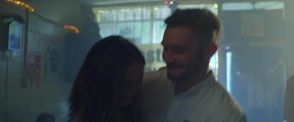A woman dancing in a bar changes dance partners as her old partner pats her new partner on the back