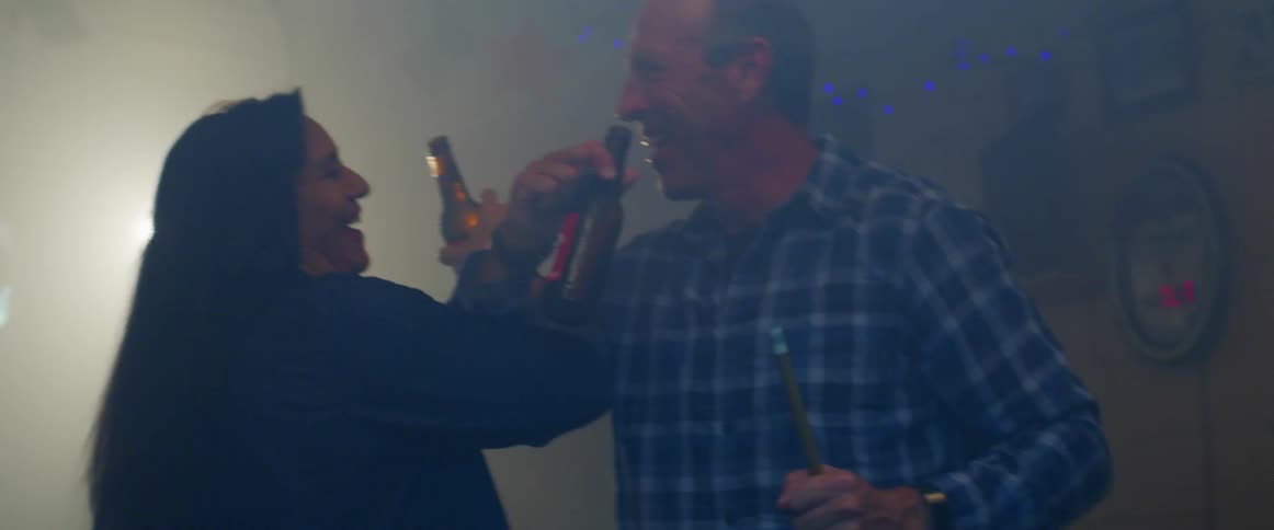 A husband and wife criss crossing arms to drink an alcoholic beverage in a bottle in a bar