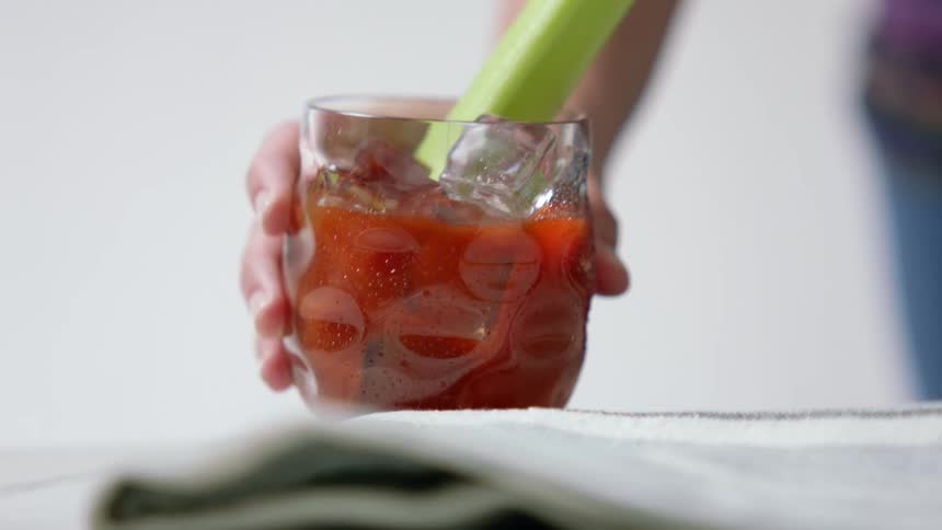Person picks up tomato juice drink with celery stalk