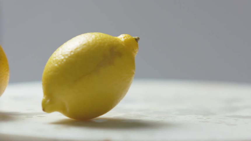 Yellow lemons falling onto a white platter