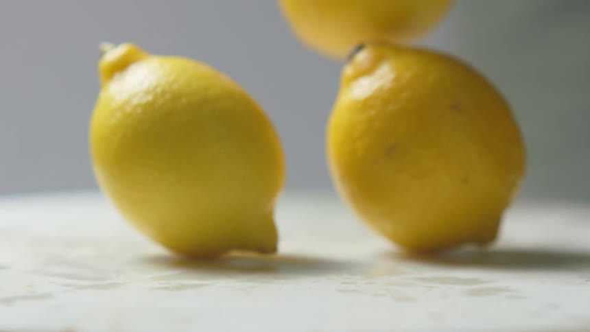 Big yellow lemons falling over a surface and bouncing out of frame