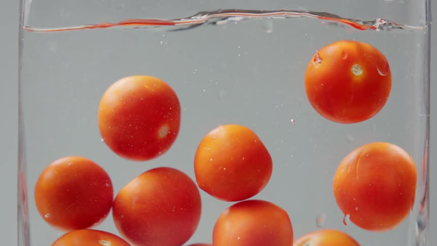Tomatoes dropping into a glass container filled with clear liquid against a grey background