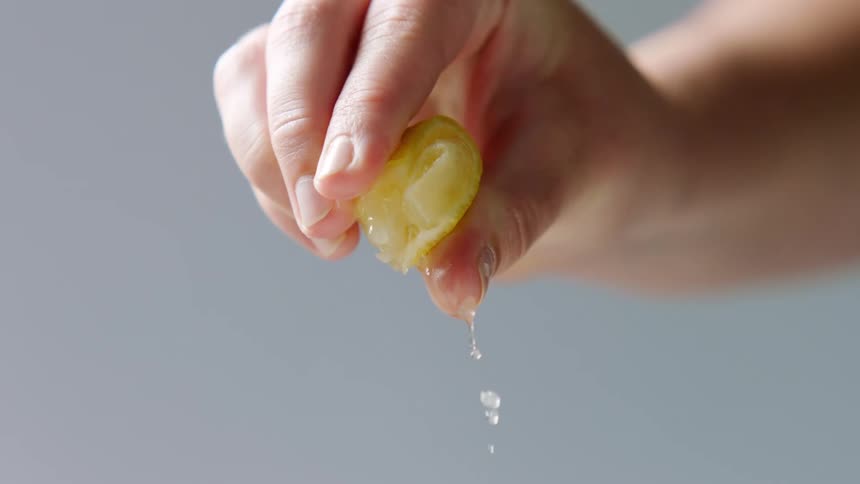 Fingers squeeze a lemon wedge causing juice to squirt out