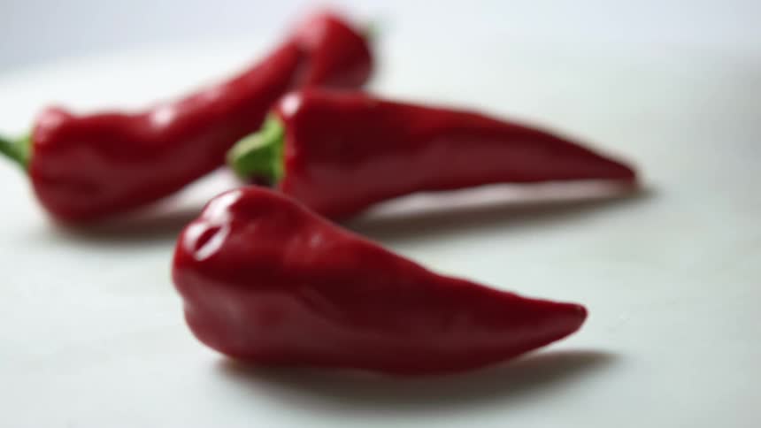 Some chili peppers with green stems are tossed on to a spinning white table