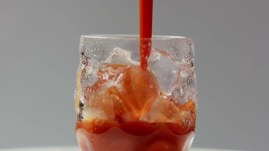 Red liquid beverage is being poured over ice into a glass that is rotating