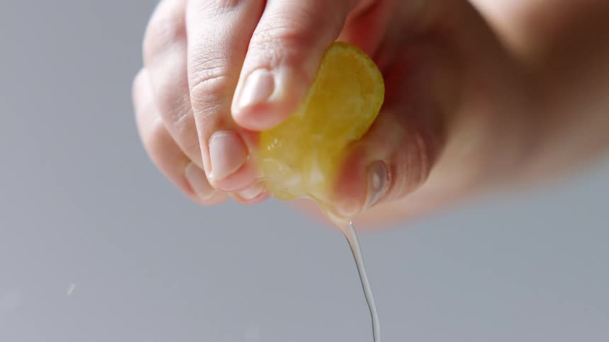 A hand squeezing a juicy yellow lemon slice
