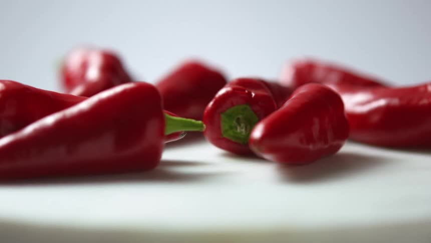 Nine red chili peppers with green stems spin on a white plate in front of a white background