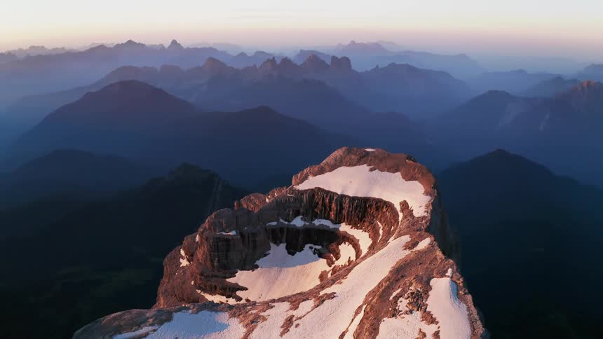 An aerial view of a snowy mountain peak in nature at sunrise