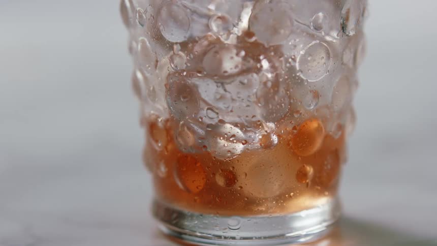 Red drink is poured into a glass with ice cubes