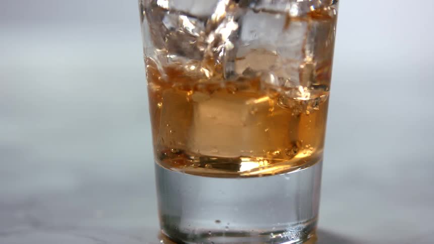 A glass with ice with a brown liquid being poured into it
