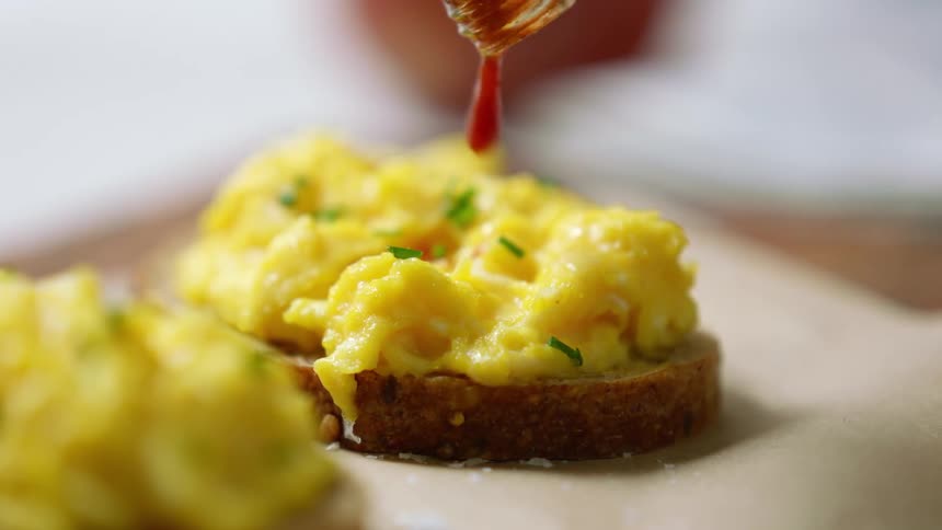 Eggs and parsley on toast with sauce being added on top from a bottle