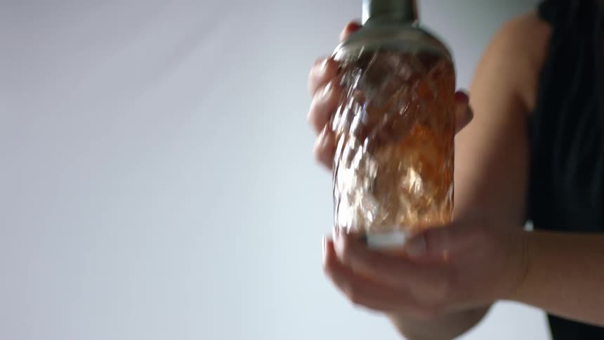 A woman shaking alcohol in a glass shaker with ice