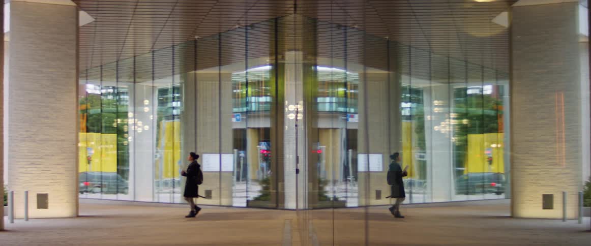 A young woman stands outside of a large building a metropolis during the day