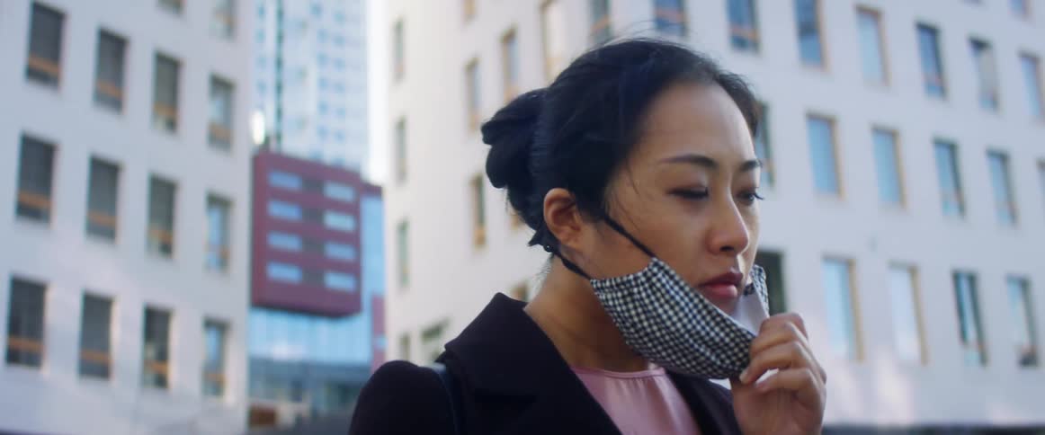 A woman takes off a black and white gingham face mask while standing outside downtown