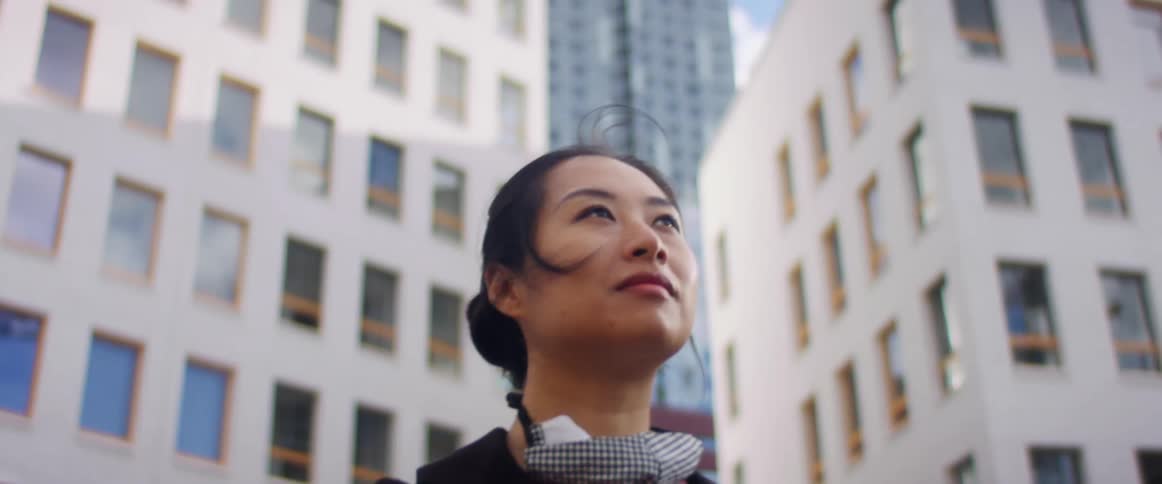 Asian woman stands near the city buildings as a covid mask hangs around her neck