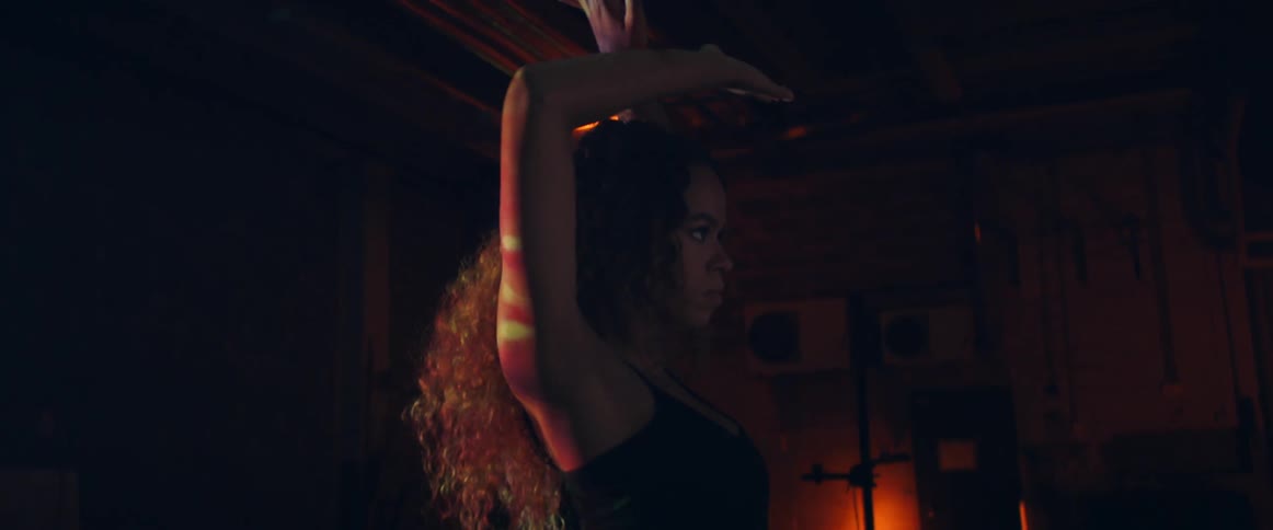 Woman dances in the shadow of dim lights wearing a tank top